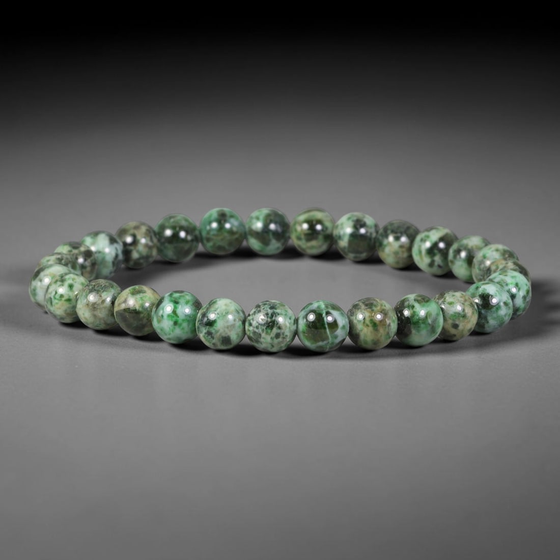 Natural Burmese Type A Variegated Speckled Green Jadeite Jade Bead Bracelet, 40TP: Strung from natural Type A Burmese jadeite, this delicate spherical bead bracelet features a variegated blend of vivid emerald green, pale celadon and earthy beige mottled speckling throughout the bea