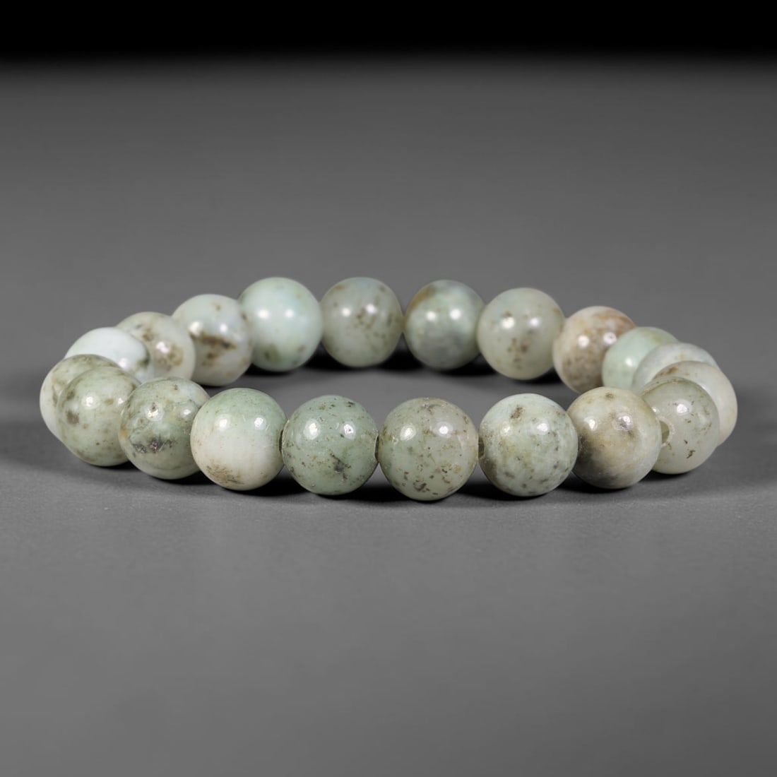 Natural Burmese Type A Speckled Pale Celadon Jadeite Jade Bead Bracelet, 99TK: Strung from natural Type A Burmese jadeite, this spherical bead bracelet carries a pale celadon ground interspersed with scattered fine dark mineral speckling across each bead surface. The beads are e