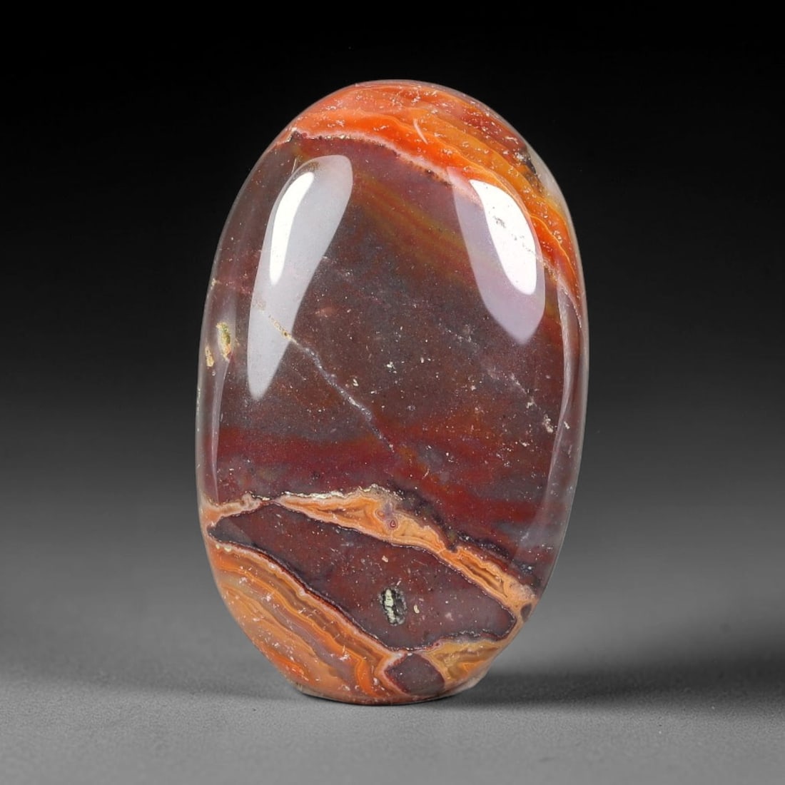 28.02ct Natural Red Banded Jasper Oval Polished Cabochon, 38TH: This polished specimen is natural red banded jasper, shaped as a smooth oval cabochon. The stone displays striking layered banding in vibrant orange, rust red and deep brown tones with subtle natural 