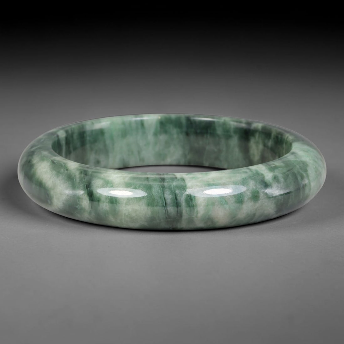 Natural Burmese Type A Banded Floating Green Jadeite Jade Bangle Bracelet, 63TD: Polished from natural Burmese jadeite, this solid bangle displays distinct layered banded striations of deep and pale floating green set against pale mineral matrix. Formed in a traditional rounded ba