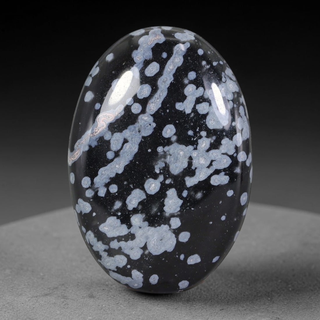 39.09 Carats Natural Snowflake Obsidian Oval Cabochon Gemstone, 34XZ: This polished domed oval cabochon measures 35.2x24.3x6.2mm, weighing a total of 39.09 carats. It features a deep glossy jet-black volcanic obsidian base, naturally adorned with abundant pale silvery-g