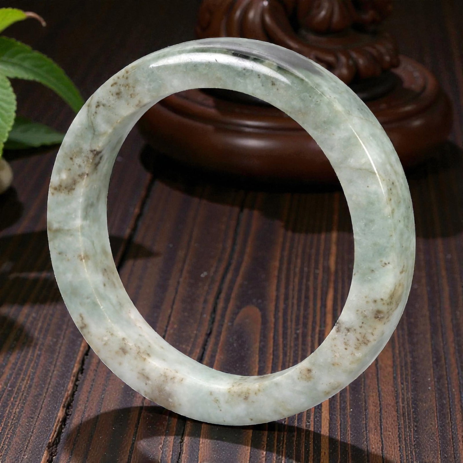 Natural Burmese Type A Jadeite Jade Bangle Bracelet, 20th Century, 87ZK: Carved from jadeite jade with a pale green base and scattered brownish inclusions, the bangle is formed as a continuous circular band with a rounded cross-section. The surface is smoothly polished, wi