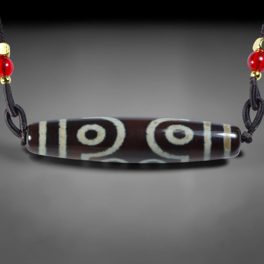 Vintage Tibetan Agate Dzi Bead Strung Pendant, 52YM: Crafted from natural agate with traditional surface patterning, this cylindrical bead has been pre-strung on a woven dark cord fitted with polished red glass accent beads and small metallic spacer bea