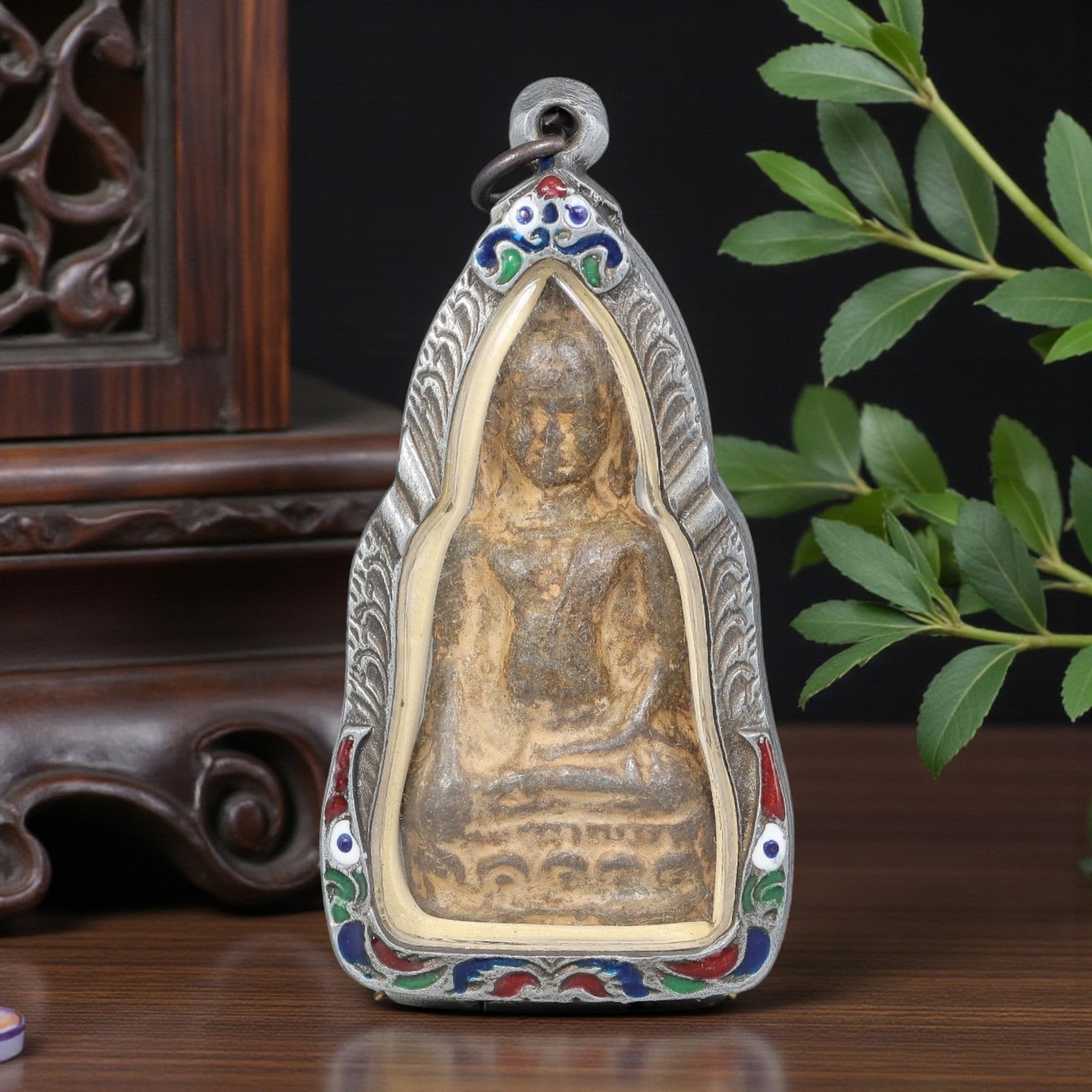 Thai Seated Buddha Amulet - Elongated Enamel Silver Tone Pendant, 51ZB: A Thai Buddhist amulet featuring a seated Buddha figure, housed in an elongated silver-tone metal casing with colorful enamel detailing. The glass-fronted enclosure protects the aged Buddha plaque, wh