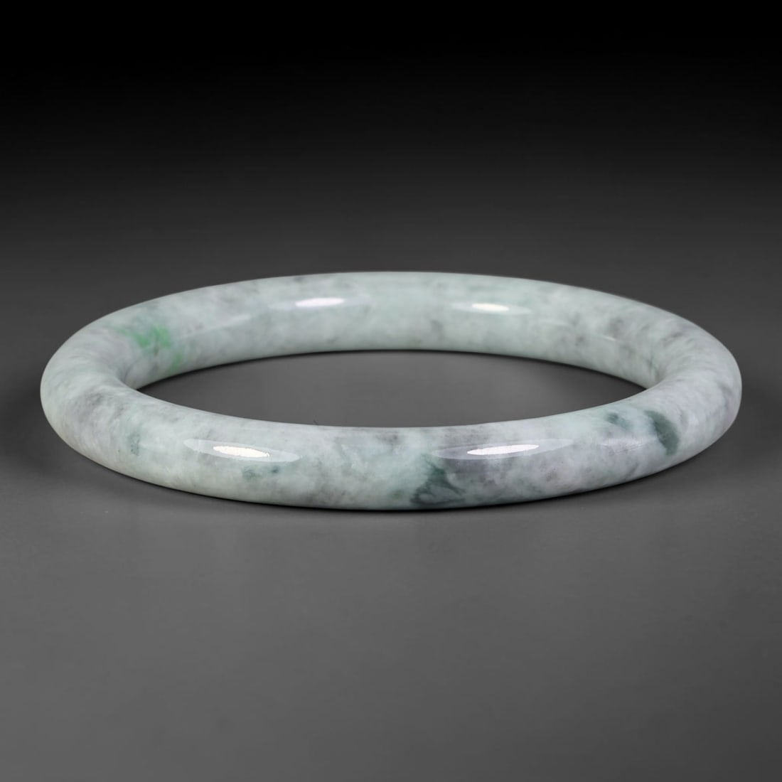 Natural Burmese Type A Jadeite Jade Bangle Bracelet, 16TD: Crafted from natural Burmese type-A jadeite, this slender bangle features a pale milky-white base blended with soft wispy grey-black clouding and subtle patches of light spring green. The hoop is smoo