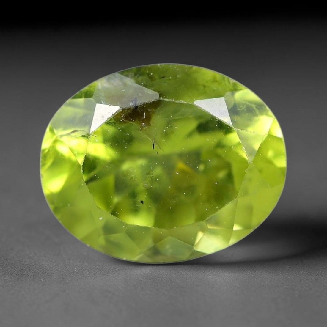 2.97ct Natural Pakistan Green Peridot Oval Faceted Gemstone, 25YW: This faceted gemstone consists of natural Pakistani peridot, fashioned into an oval cut with polished facets that highlight its vivid green body colour. Natural mineral inclusions are visible within t