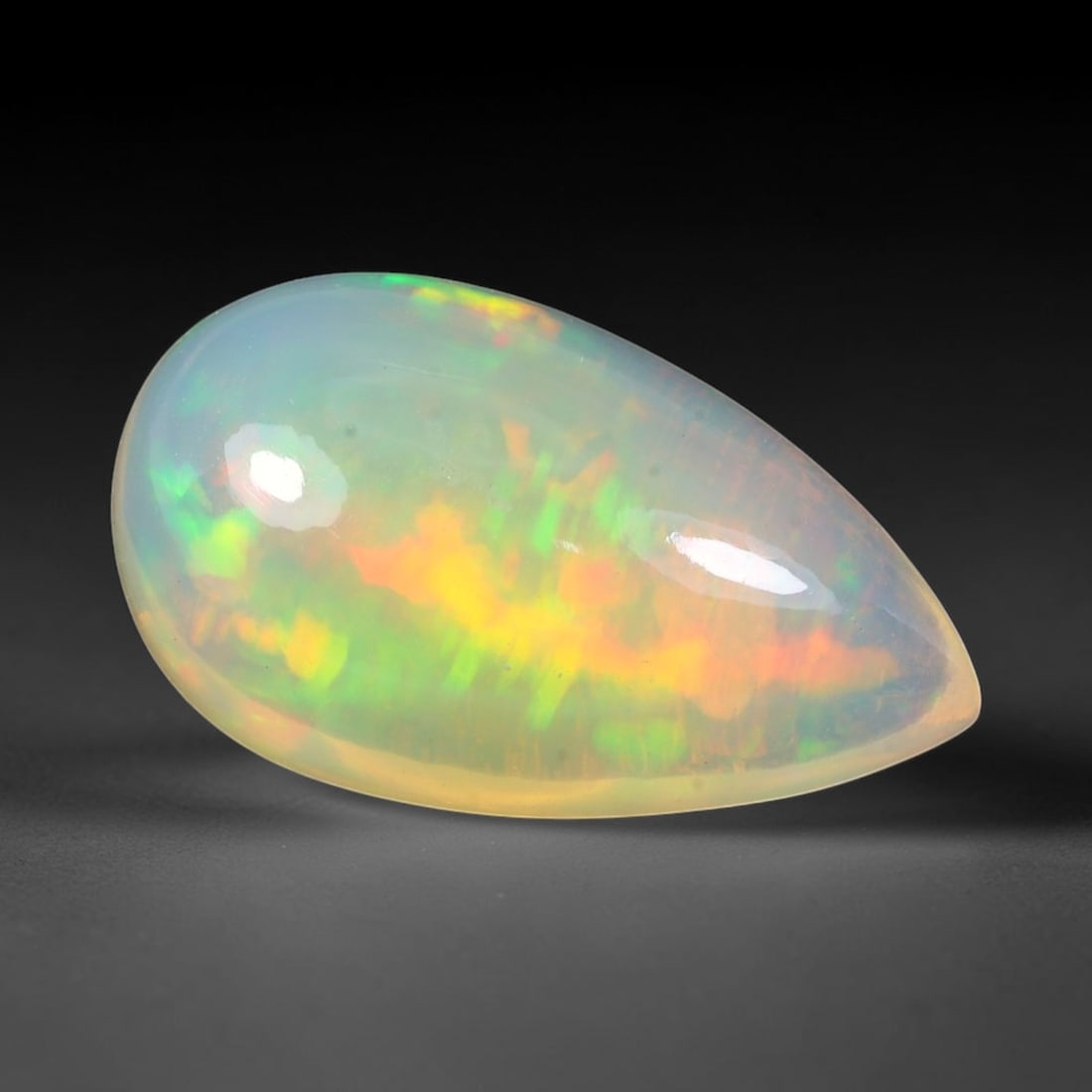 7.84ct Natural Ethiopian Welo Solid Opal Pear Cabochon, 1TG: This natural solid opal cabochon originates from Ethiopia Welo. The translucent pale base exhibits striking play-of-color with flowing bands of vivid green, golden yellow and warm orange across the po