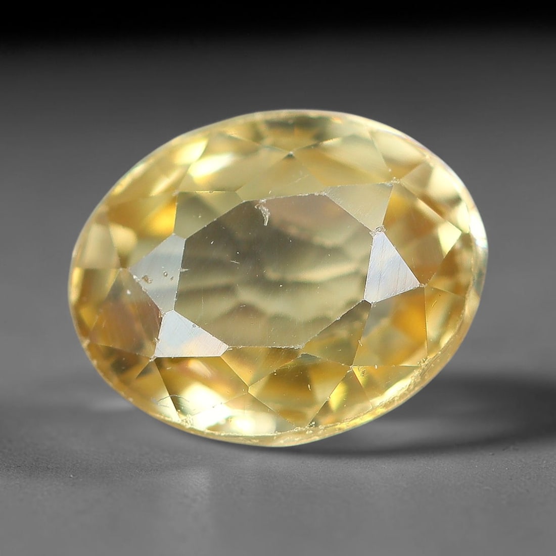 2.04ct Natural Pale Golden Yellow Zircon Oval Cut Loose Gemstone, 18TM: This faceted specimen is natural zircon, fashioned in an oval brilliant cut. The stone displays a translucent pale golden yellow hue, with visible internal inclusions and fine surface traces consisten