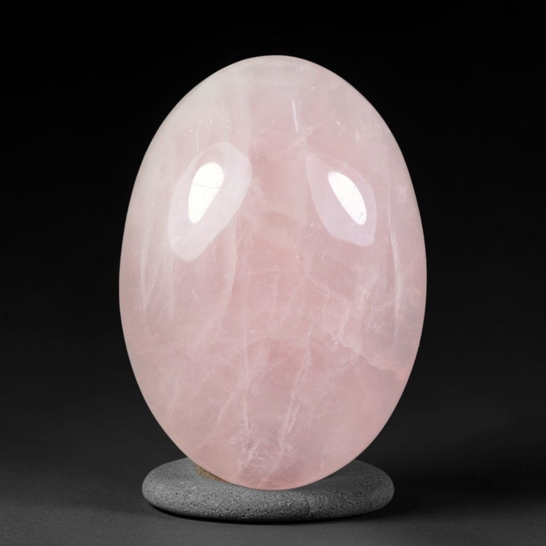 105.27ct Natural Rose Quartz Oval Polished Palm Stone, 39TH: This polished specimen is natural rose quartz, shaped into a smooth oval palm stone. The stone features a soft pale pink hue with subtle natural veining visible throughout the translucent crystal matr