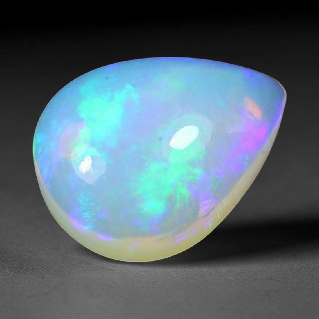 5.98ct Natural Ethiopian Welo Solid Opal Pear Cabochon, 7TG: This natural solid opal cabochon originates from Ethiopia Welo. The translucent pale base presents beautiful play-of-color with bright cyan green, sky blue and soft purple iridescent flashes across th