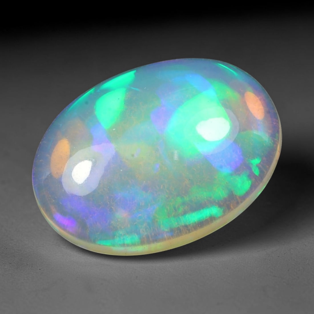 6.86ct Natural Ethiopian Welo Solid Opal Oval Cabochon, 8TG: This natural solid opal cabochon originates from Ethiopia Welo. The translucent pale base displays bright play-of-color with vivid green, blue, purple and warm orange iridescent flashes across the pol