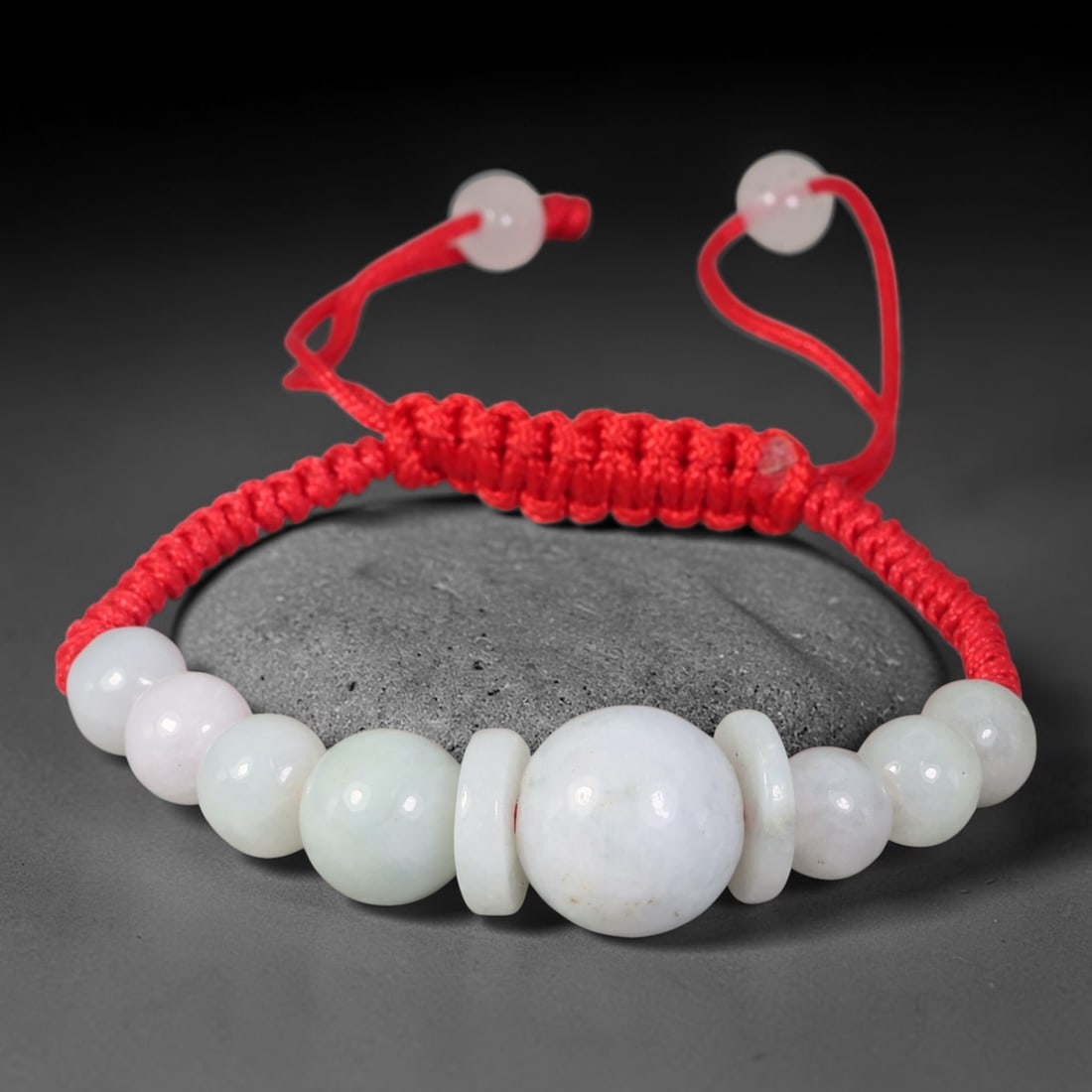 Natural Burmese Type A Milky White Graduated Jadeite Adjustable Red Braided Cord Bracelet, 18TP: Handcrafted adjustable red braided cord bracelet, composed of natural Type A Burmese jadeite graduated round beads in milky white with subtle pale celadon undertones. A large central focal bead is fra