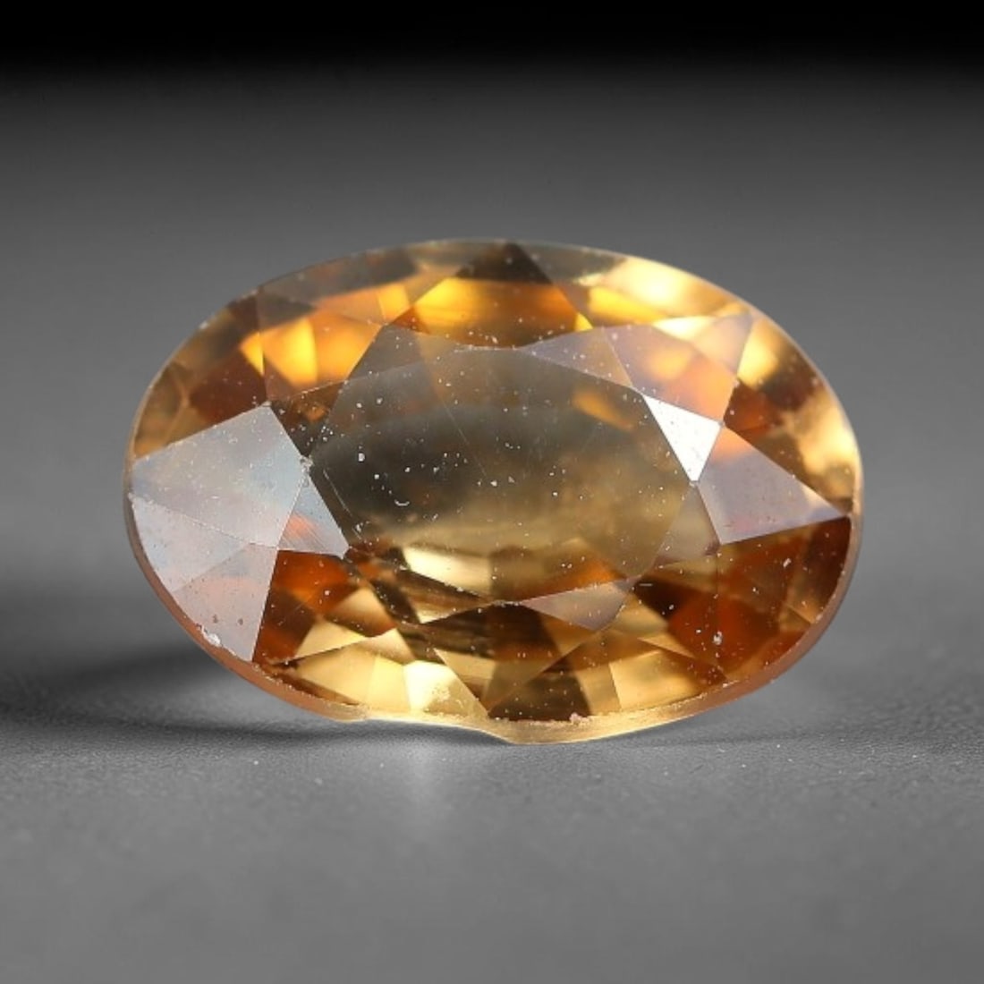 2.69ct Natural Golden Brown Zircon Oval Cut Loose Gemstone, 13TM: This faceted specimen is natural zircon, fashioned in an oval brilliant cut. The stone exhibits a translucent golden brown hue, with fine particulate inclusions visible within the crystal matrix. Face