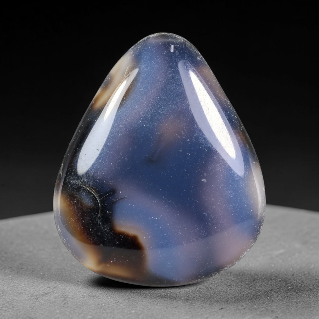 94.01ct Natural Banded Onyx Teardrop Polished Cabochon, 41TH: This polished specimen is natural banded onyx, shaped as a smooth teardrop cabochon. It features soft hazy blue-grey areas blended with warm brown and creamy banding within a translucent matrix. The s