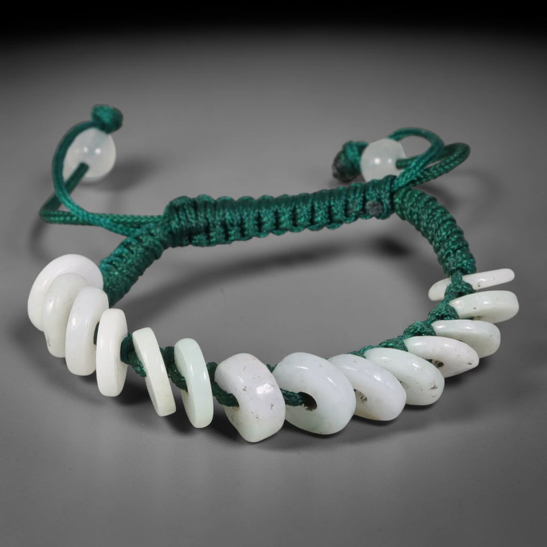 Natural Burmese Type A Off-White Donut Jadeite Adjustable Braided Cord Bracelet, 21TP: Handcrafted adjustable deep green braided cord bracelet, adorned with natural Type A Burmese jadeite donut beads in soft off-white hue. The flat disc beads carry faint natural mineral speckles and sub