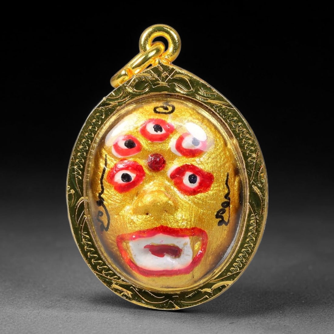 Thai Five-Eyed Golden Face Votive Amulet - Gold Cased Pendant, 11YY: Teardrop oval shaped devotional pendant enclosed in finely engraved polished gold casing with transparent protective dome and integrated hanging bail. One side features a vivid golden five-eyed deity 