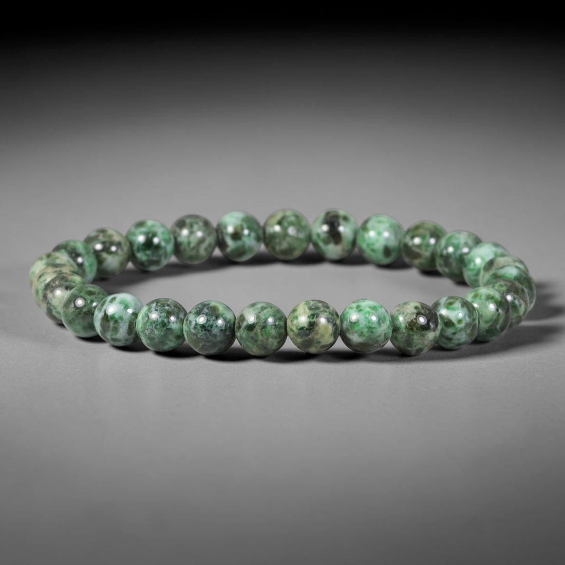 Natural Burmese Type A Speckled Green Mottled Jadeite Jade Bead Bracelet, 33TP: Strung from natural Type A Burmese jadeite, this slender spherical bead bracelet displays rich mottled forest green interspersed with pale celadon and dark mineral speckles across each bead. Every bea