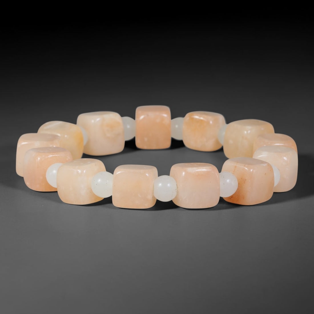 Natural Peach Calcite Cube Beaded Bracelet with White Jadeite Spacers, 50TP: Polished elastic strand bracelet hand-strung with soft peach-toned calcite cube beads, divided by smooth round white jadeite spacer beads. Gentle natural tone variations and faint internal veining run
