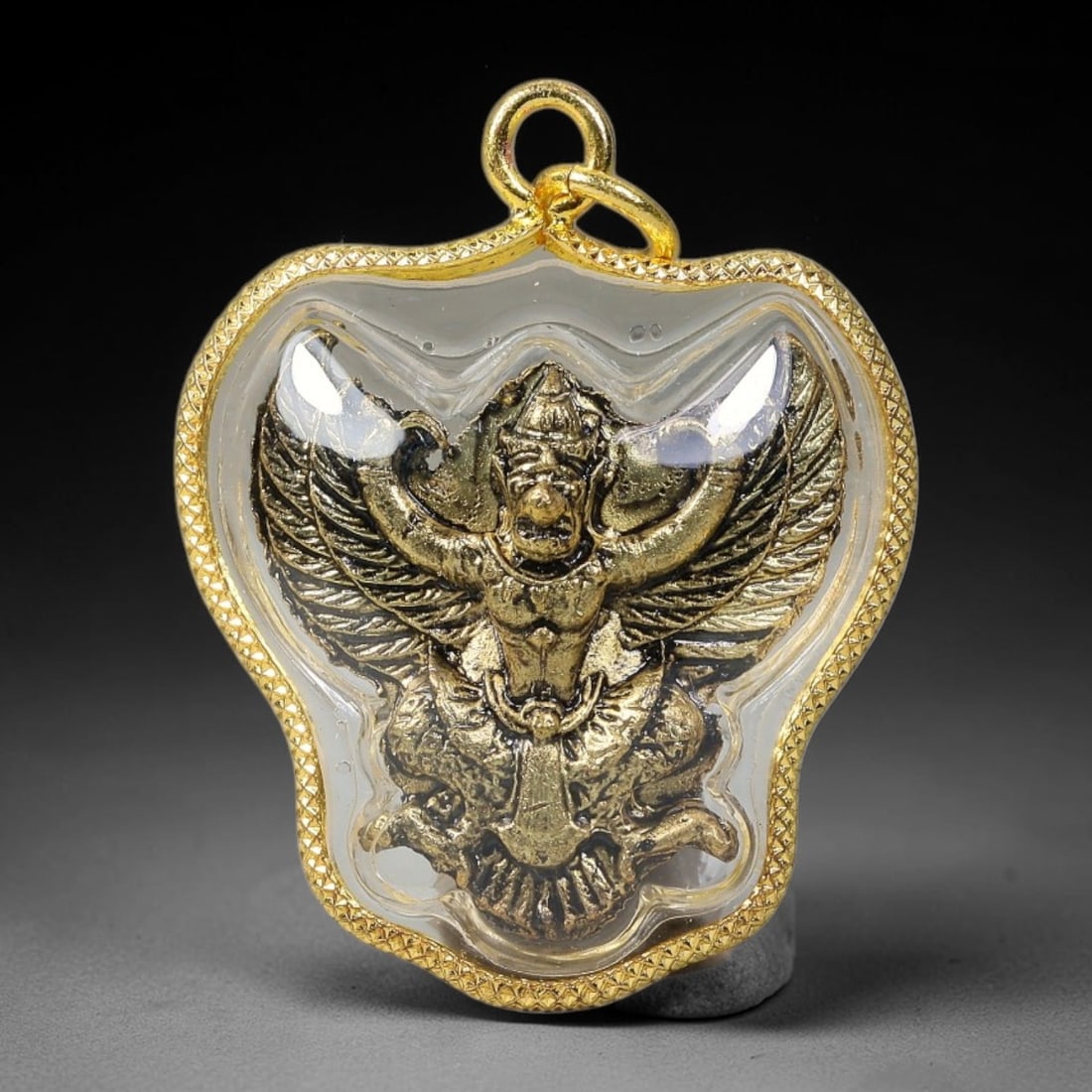 Thai Gold Plated Garuda Bird God Amulet Pendant With Clear Waterproof Casing, 65YY: Bat-wing shaped textured gold frame amulet measuring 4.0x3.0cm, fitted with double gold jump rings for easy necklace attachment. Sealed transparent protective cover encloses an antique gold-toned embo
