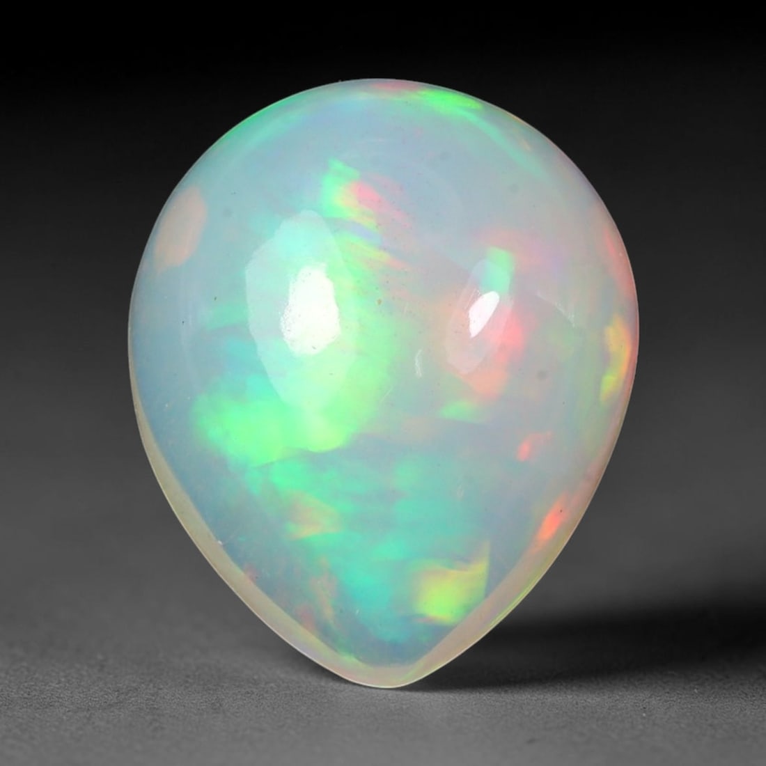7.36ct Natural Ethiopian Welo Solid Opal Pear Cabochon Loose Gemstone, 14TG: Solid opal cabochon mined from Ethiopia's Welo opal fields, fashioned into a smooth pear teardrop silhouette with a glossy polished dome. The translucent milky host matrix exhibits vibrant shifting pl