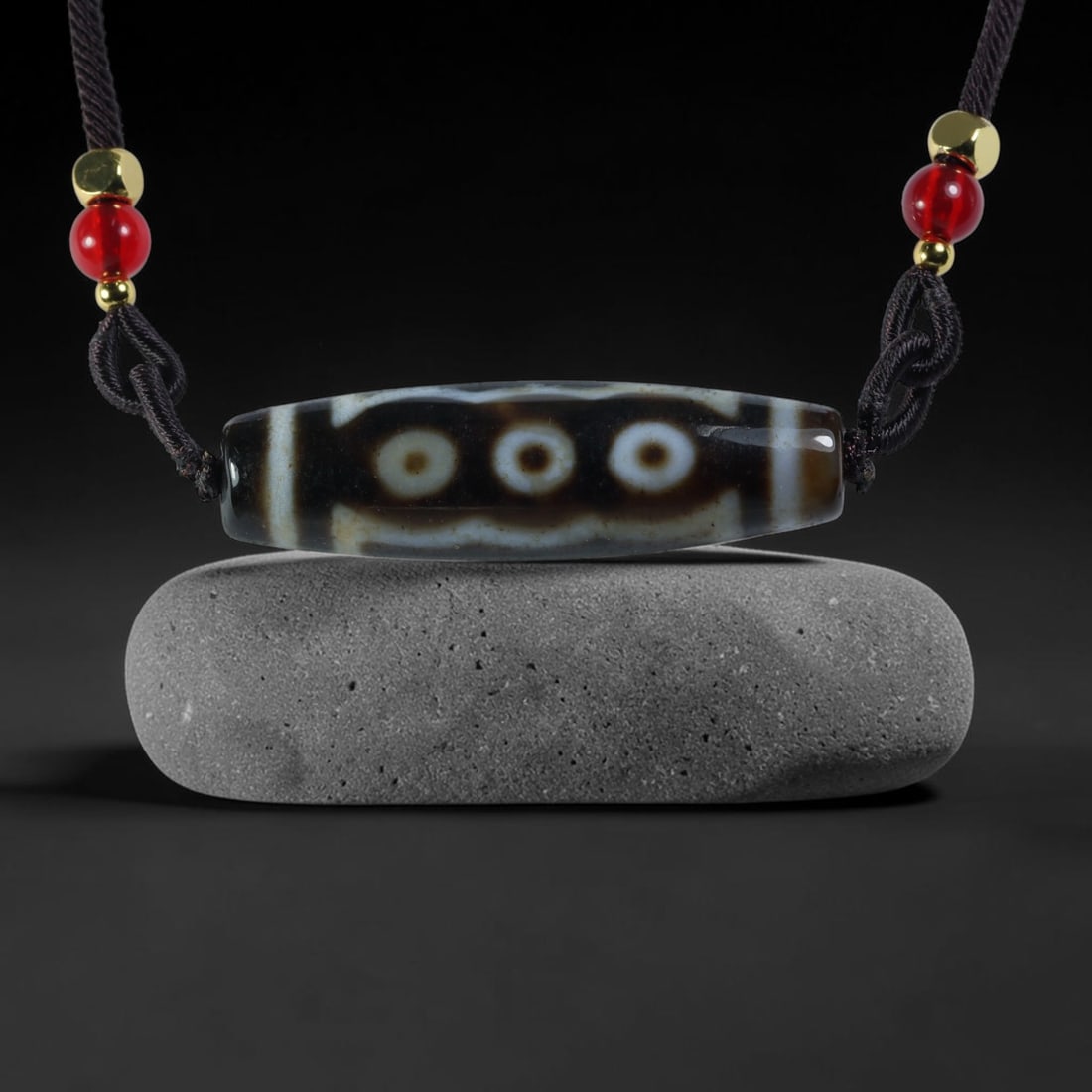 Vintage Tibetan Agate Dzi Bead Strung Pendant, 48YM: Crafted from natural agate with traditional surface patterning, this cylindrical bead has been pre-strung on a woven dark cord fitted with polished red glass accent beads and small metallic spacer bea