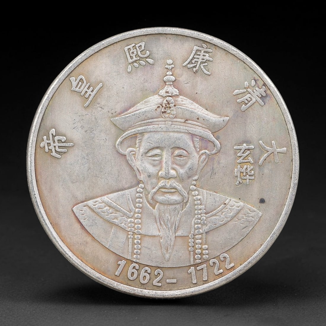 A Chinese Metal Commemorative Coin - Kangxi Emperor Dragon Medallion, 54ZQ: Cast base-metal medallion with double-sided relief ornamentation. The obverse presents a bust portrait of the Kangxi Emperor dressed in formal Qing imperial ceremonial headdress and court robes, encir