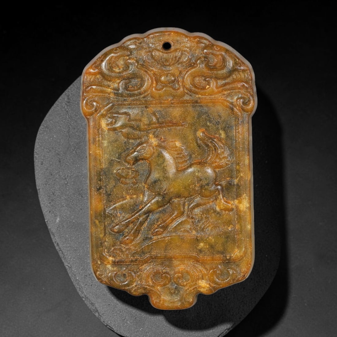 A Chinese Relief-Carved Mottled Yellow-Brown Jade Stone Running-Horse Plaque Pendant, 92YF: Decorative shaped-border jade plaque pendant with a suspension hole drilled at the top for cord attachment. The obverse features finely worked relief carving of a galloping horse, framed by ornate scr