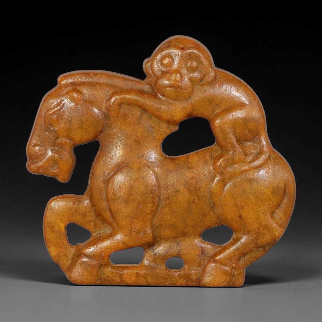 A Chinese Open-Work Carved Russet-Orange Jade Stone Monkey-On-Horse Pendant, 100YF: Stylized open-work jade pendant depicting a monkey perched atop a horse, rendered with multiple pierced cut-outs to define the forms. Fine surface carving details the facial features and body contours