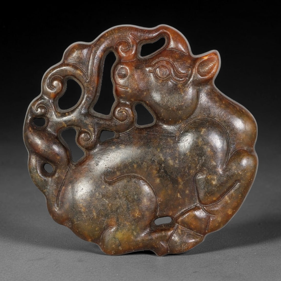 A Chinese Open-Work Carved Jade Stone Ox Pendant, 71WT: Finely worked open-work jade pendant with rich mottled brown-green tone. The obverse features a reclined ox figure intertwined with scrolling ornamental motifs, executed in relief carving with multipl