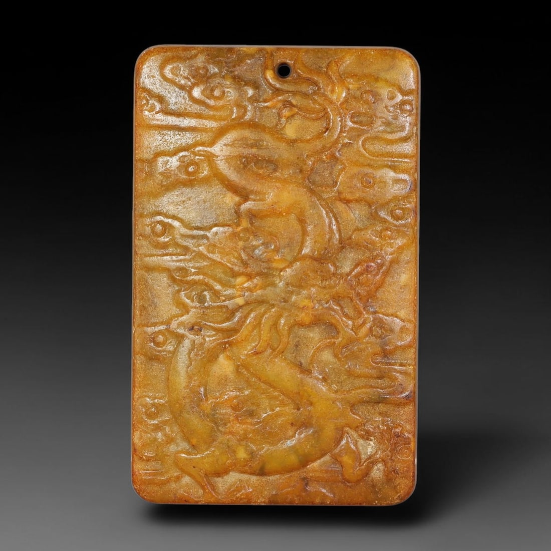 A Chinese Relief-Carved Yellow-Brown Jade Stone Dragon Plaque Pendant, 91YF: Rectangular jade plaque pendant with smoothly rounded corners. The obverse features detailed relief carving of a coiled dragon amid swirling cloud motifs. A suspension hole is drilled at the top for t