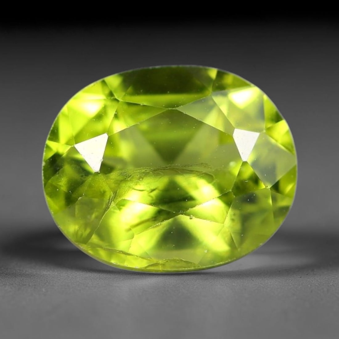 3.19ct Natural Pakistan Green Peridot Oval Faceted Gemstone, 26YW: This faceted gemstone consists of natural Pakistani peridot, fashioned into an oval cut with polished facets that highlight its vivid green body colour. Natural mineral inclusions are visible within t