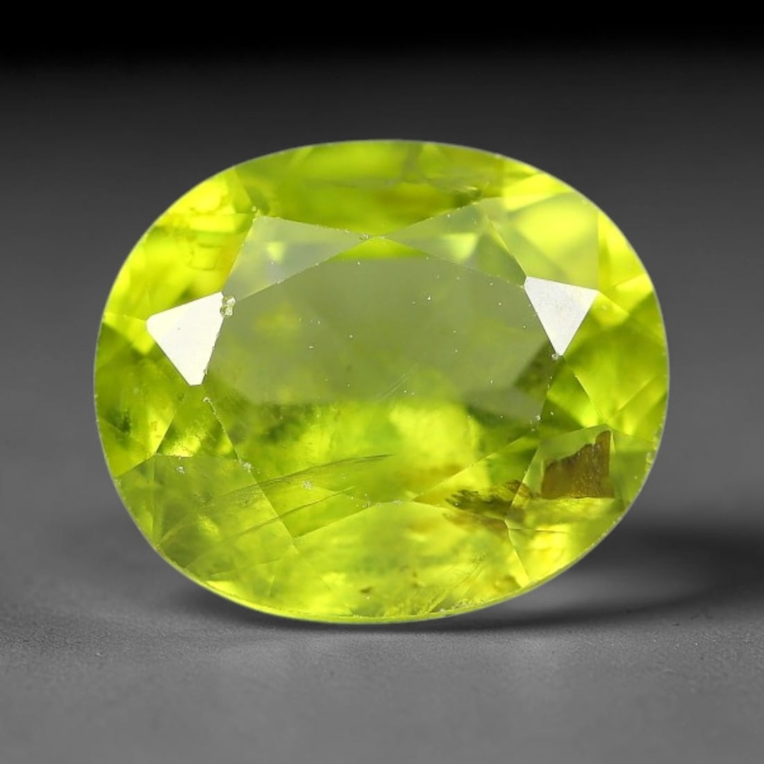 3.37ct Natural Pakistan Green Peridot Oval Faceted Gemstone, 21YW: This faceted gemstone consists of natural Pakistani peridot, fashioned into an oval cut with polished facets that highlight its vivid green body colour. Natural mineral inclusions are visible within t