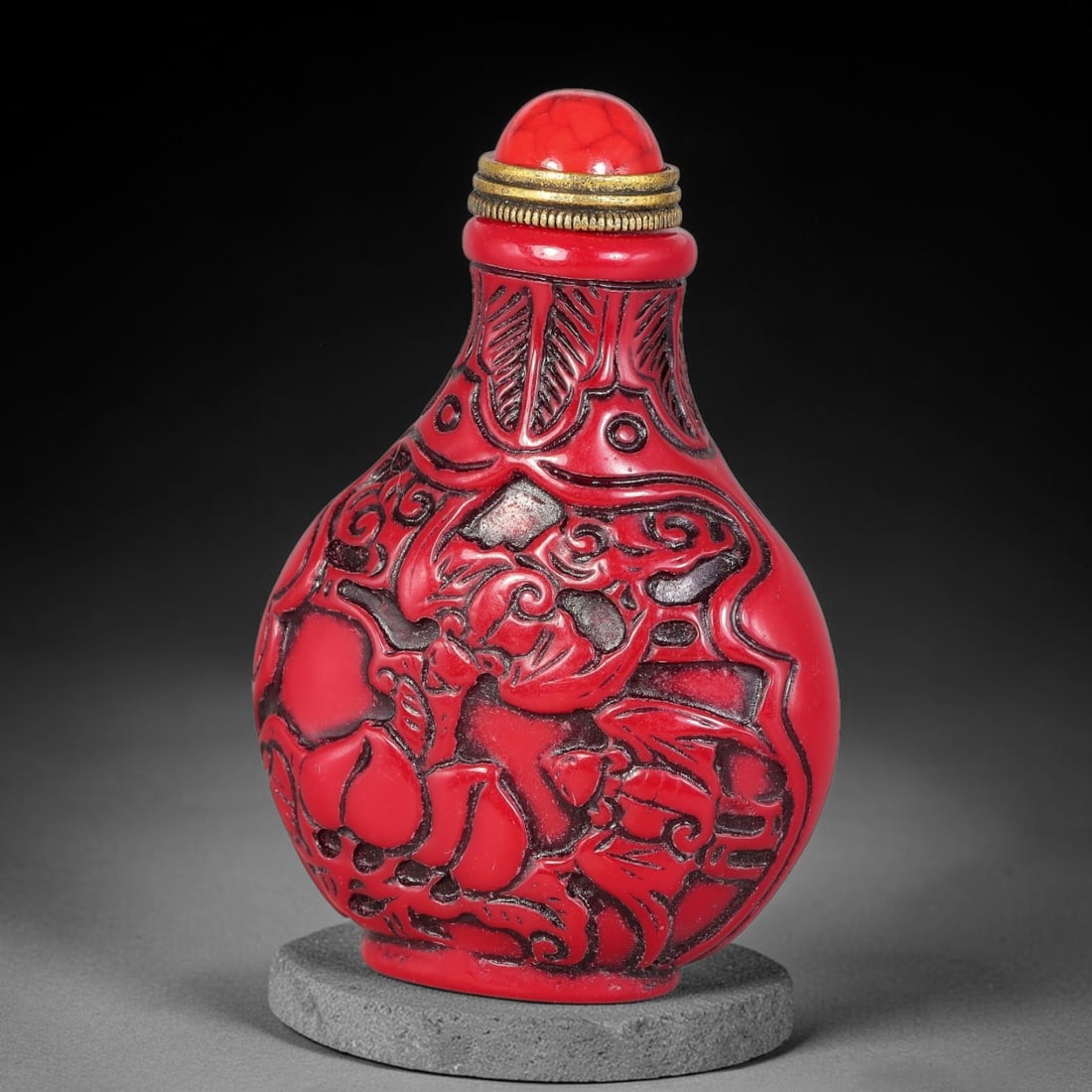 A Chinese Carved Red Snuff Bottle with Auspicious Relief Motifs, 29ZQ: Bulbous-form snuff bottle crafted in vibrant red material, fitted with a red cracked-texture stopper and brass-toned metal fitting. Both sides are decorated with deep relief carvings featuring traditi