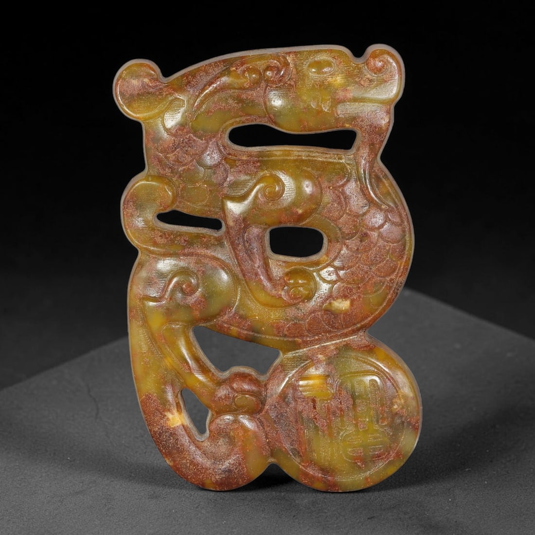 A Chinese Open-Work Carved Jade Stone Dragon Pendant, 74WT: Vertically oriented open-work jade pendant showcasing an intricately carved coiled dragon figure with fine scale relief details. One section bears incised emblematic character decoration. The stone di