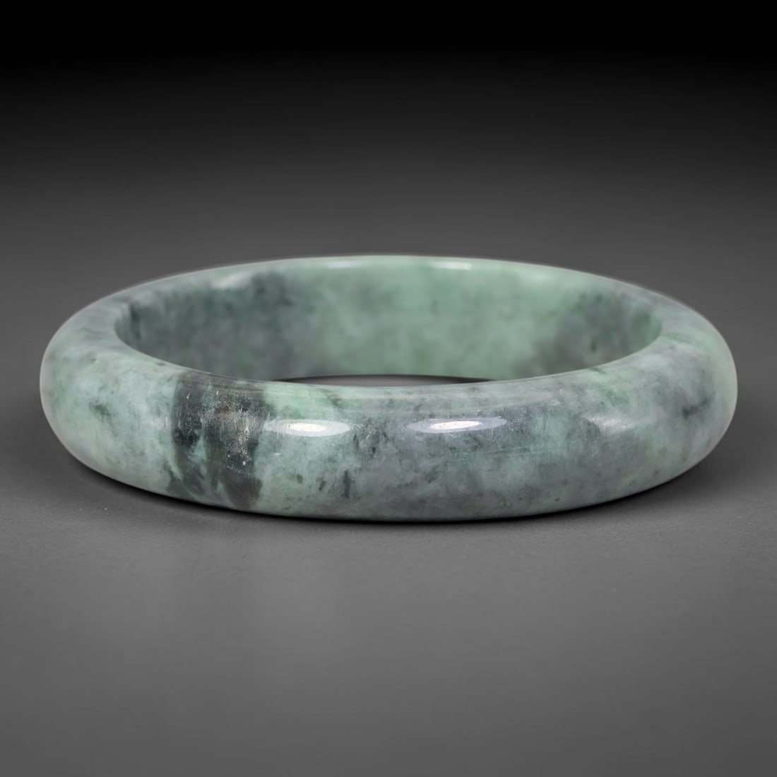 Natural Burmese Type A Moss Floating Green Jadeite Jade Bangle Bracelet, 29TD: This thick band bangle is crafted from natural Burmese Type A jadeite. The stone displays a muted soft green base with prominent dark mossy mineral inclusions sweeping across the surface. The bangle h