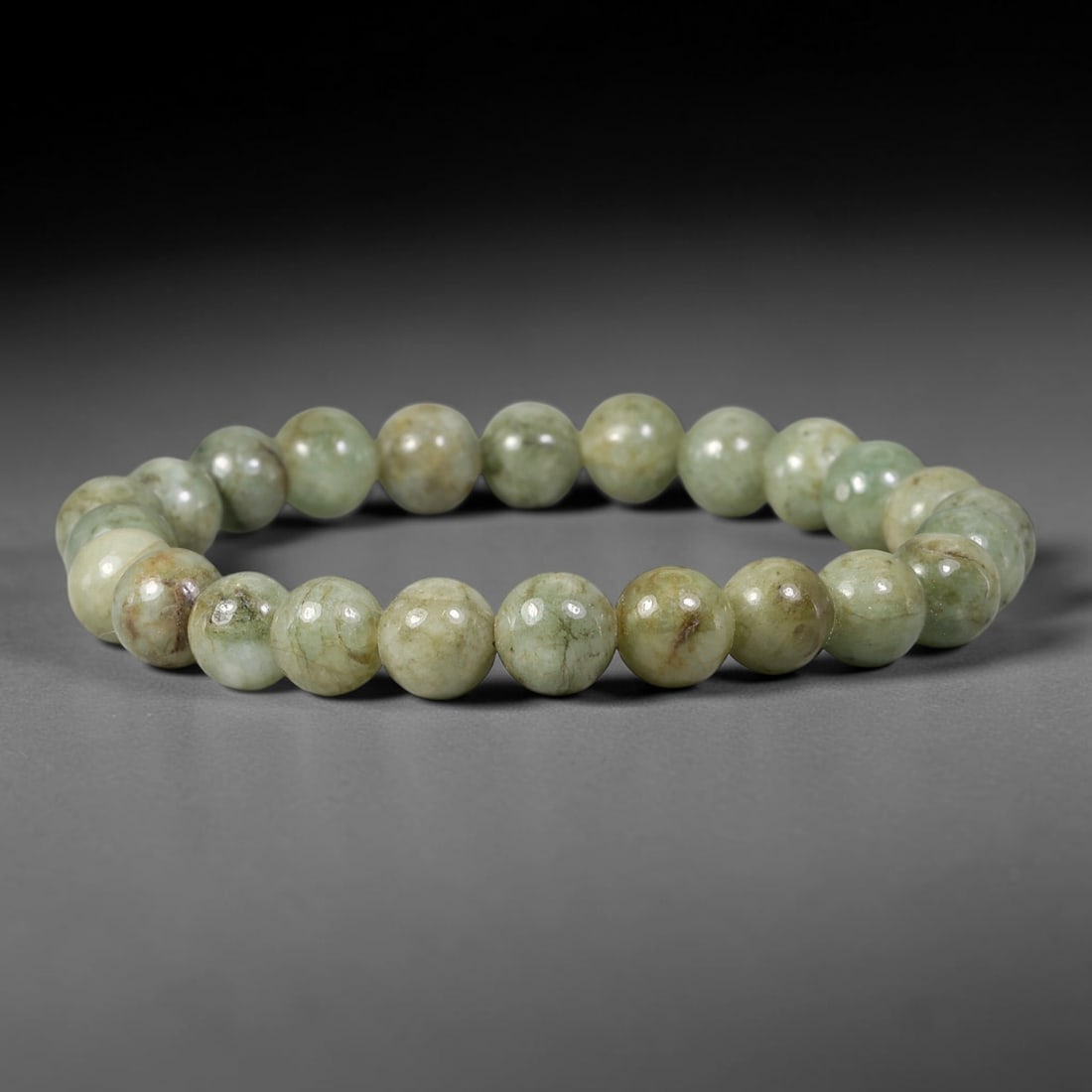 Natural Burmese Type A Mossy Variegated Jadeite Jade Bracelet, 66TK: Hand-strung bracelet with polished round natural Burmese Type A jadeite beads measuring 7.8mm. The beads feature muted pale celadon green base with natural earthy brown veining and mottled inclusions.