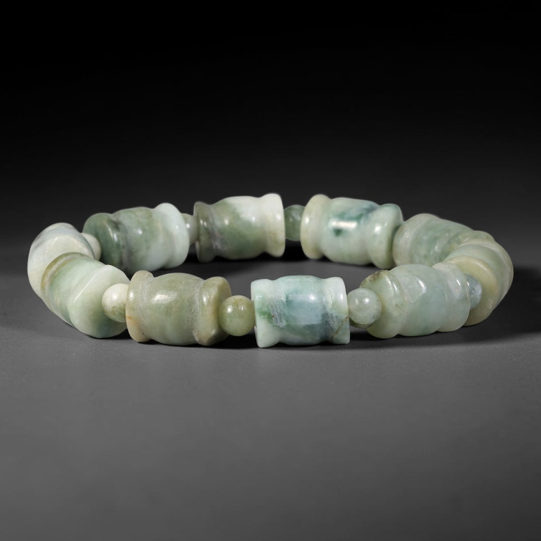 Natural Burmese Type A Carved Barrel Jadeite Jade Bracelet, 58TK: Hand-strung bracelet with carved barrel-shaped natural Burmese Type A jadeite beads measuring 11.7mm. The beads exhibit rich deep green blended with earthy muted tones and natural dark mottling. Small