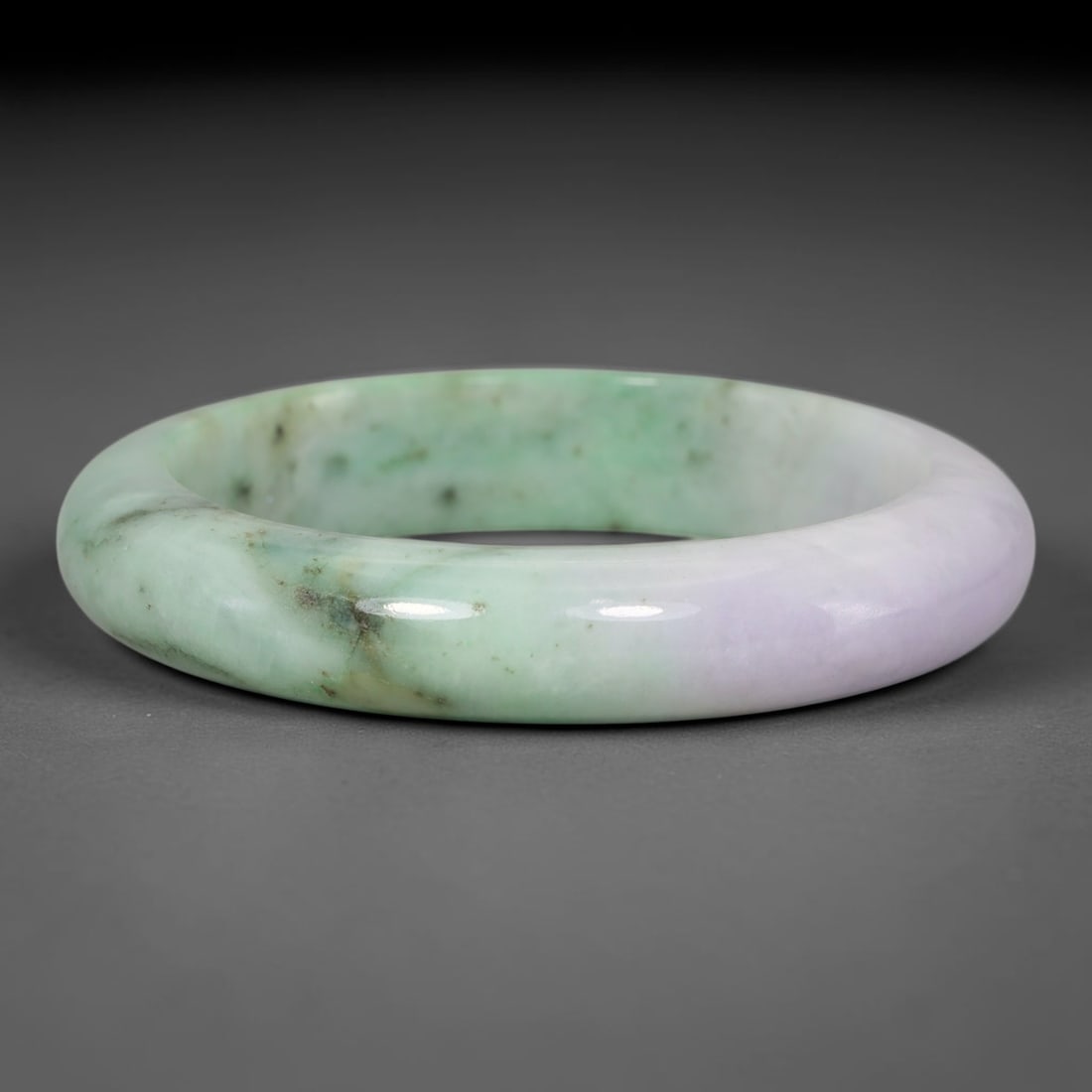 Natural Burmese Type A Lavender Green Speckled Jadeite Jade Bangle Bracelet, 26TD: This solid band bangle is crafted from natural Burmese Type A jadeite. The stone features a pale lavender section transitioning into soft mint green, accented by scattered dark speckled mineral inclus