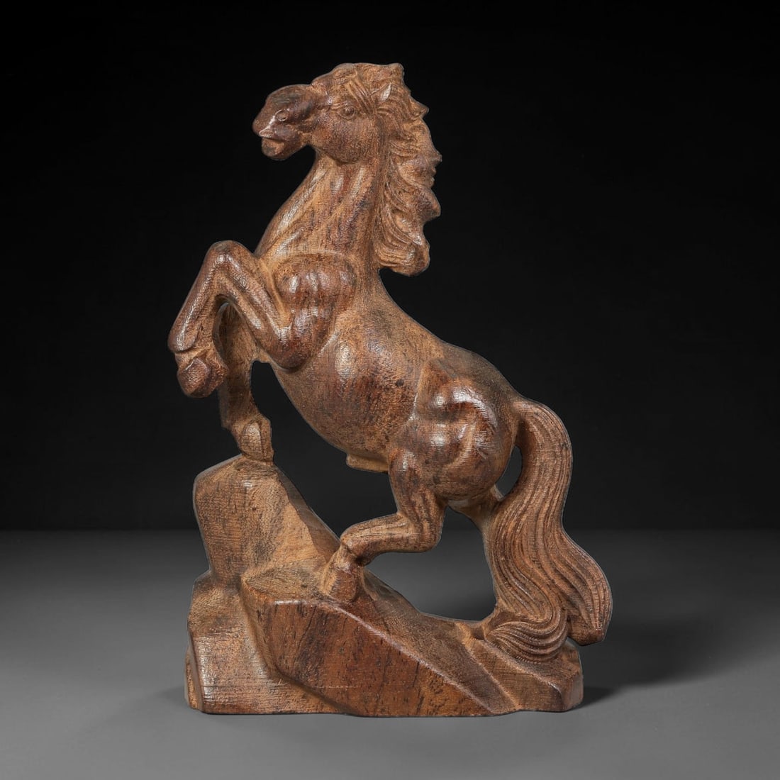 A Carved Agarwood Figure of a Rearing Horse Sculpture Figurine, 3SD: Carved from fragrant agarwood (Aquilaria spp.), the work depicts a horse rearing upon a rugged rocky base, front legs raised and head held high with windswept layered mane. The musculature of the body