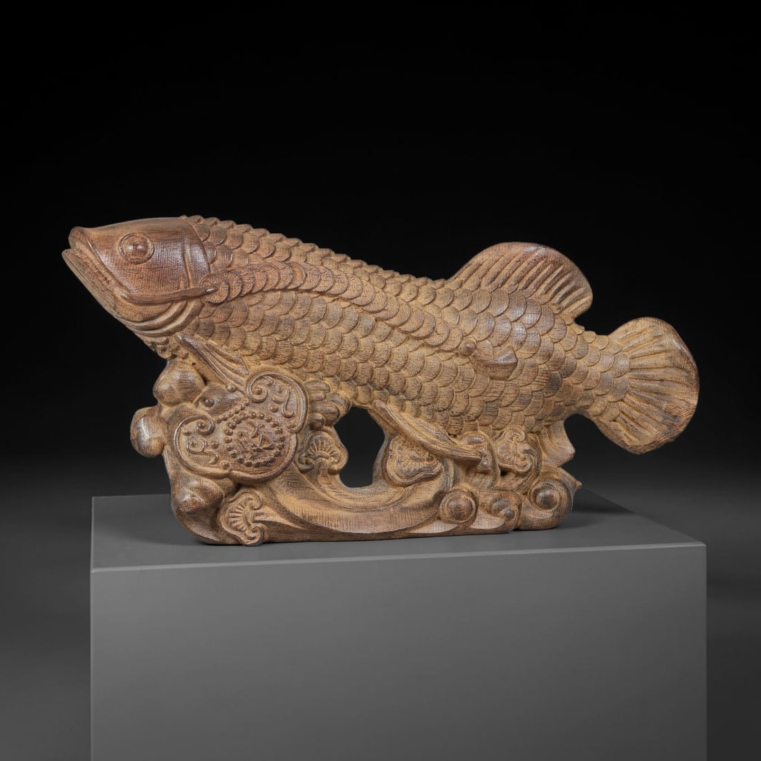 A Carved Agarwood Figure of a Fish Sculpture Figurine, 2SD: Carved from fragrant agarwood (Aquilaria spp.), the work depicts a large fish resting upon swirling wave and ruyi ornament base. Individual scales are meticulously rendered across the body, with defin