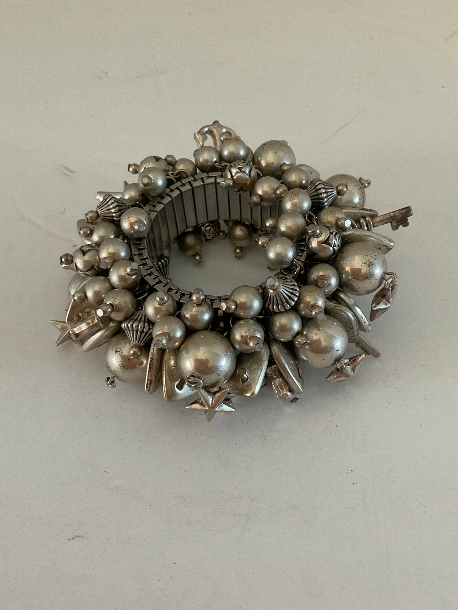 Vintage Silver Tone Cha Cha Charm Bracelet: A metal stretch vintage Cha Cha bracelet. This piece features multiple charmes, hearts, stars, balls, keys and more. Fun piece that stretches to fit. Good condition