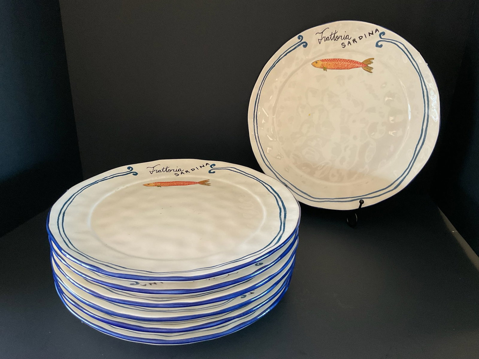 Set of Trattoria Sardina Dinner Plates from Anthropologie: A set of seven dinner plates from Anthropologie. Each features an orange sardine and a rippled surface. They have a bit of crackling, otherwise good conditon. Each is 11" in diameter.