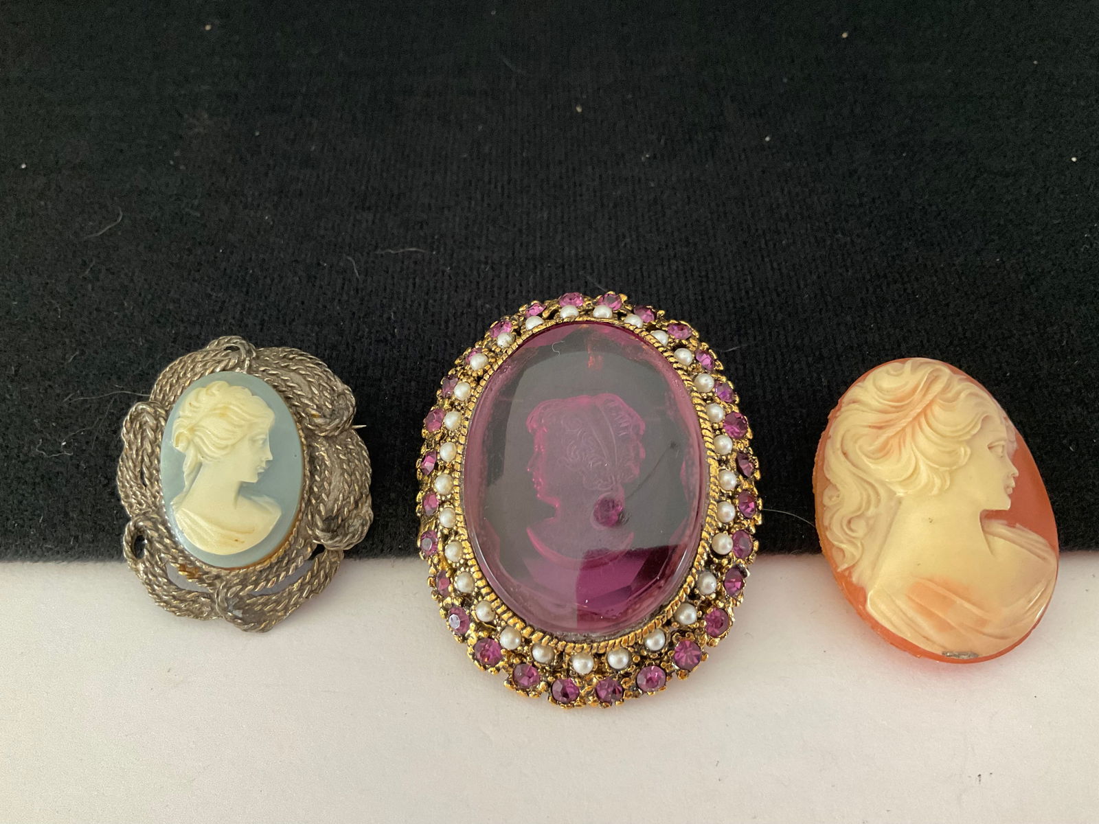 Assortment of Three Vintage Cameos and a Painted Piece: A collection of three cameo pieces. Included is an intaglio carved cameo set in large purple glass with faux pearl accents, two traditional carved cameos, only one is in setting. Also included is a pa