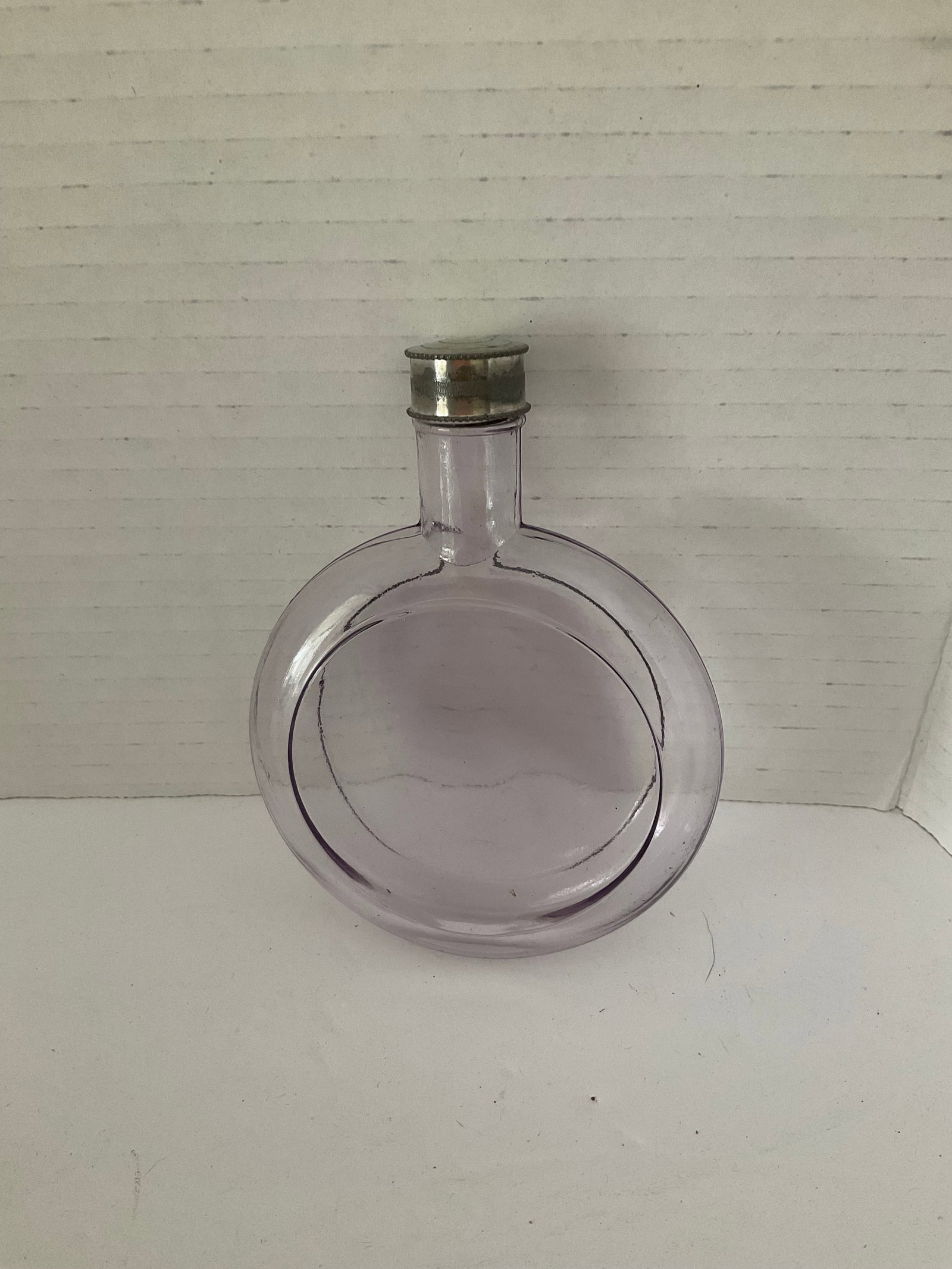Antique Glass Pocket Flask: An antique glass pocket flask with silver tone top. It has a sun drenched lavender hue. These were used during prohibition to hide libations. It measures 5" x 3.5" x 1".