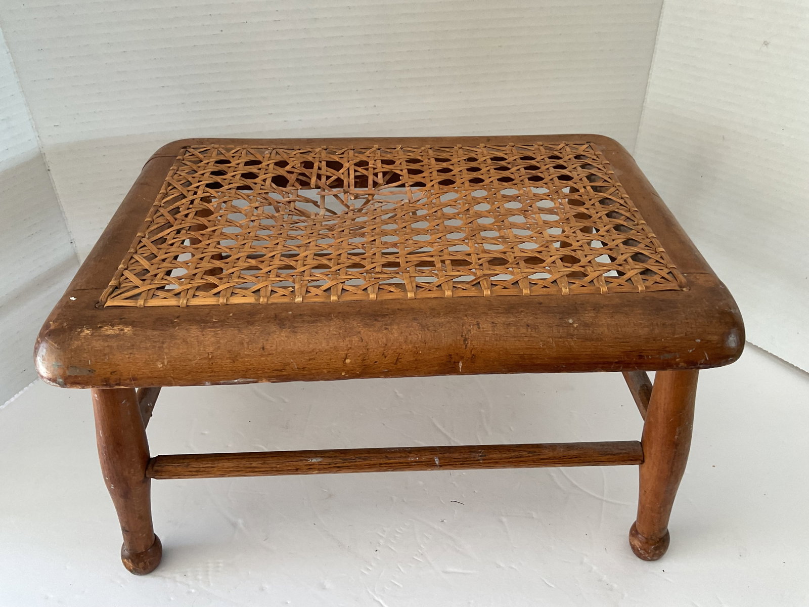 Antique Wood and Caned Foot Stool: An antique wood foot stool with caned top. The top needs a repair as shown in photo. Nice turned legs. It measures 8”h x 9”w x 13”.