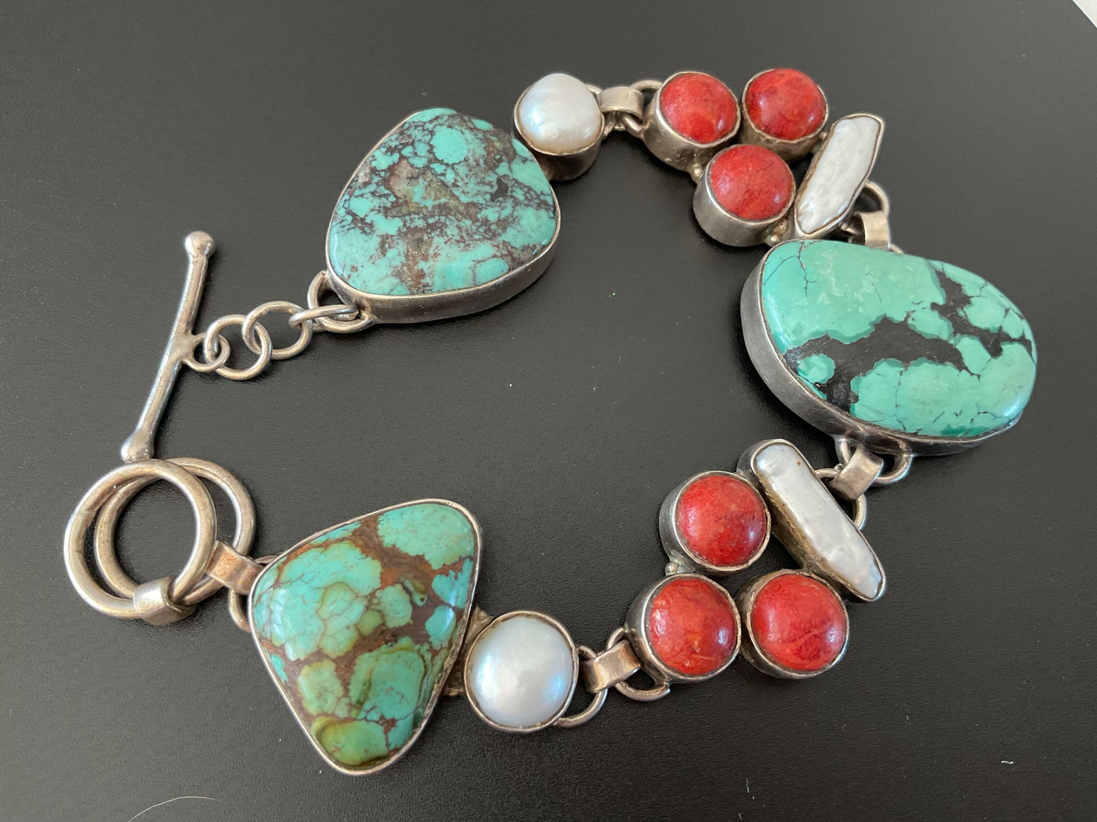 Stamped Vintage Sterling, Turquoise, Coral and MOP Bracelet: A chunky vintage Southwestern style bracelet. The bracelet has a toggle closure with turquoise, coral and mother of pearl accents. It is 7.5" in length and weighs all inclusive 63.1 grams.