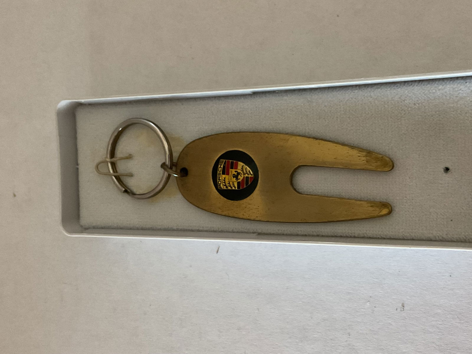 Porche Metal Key Ring with Golf Divot Repair Tool: A vintage Porche Key ring with Stuttgart Porche coat of arms. The keyring holds a goldtone golf divot repair tool. 5" in length. Comes with box.