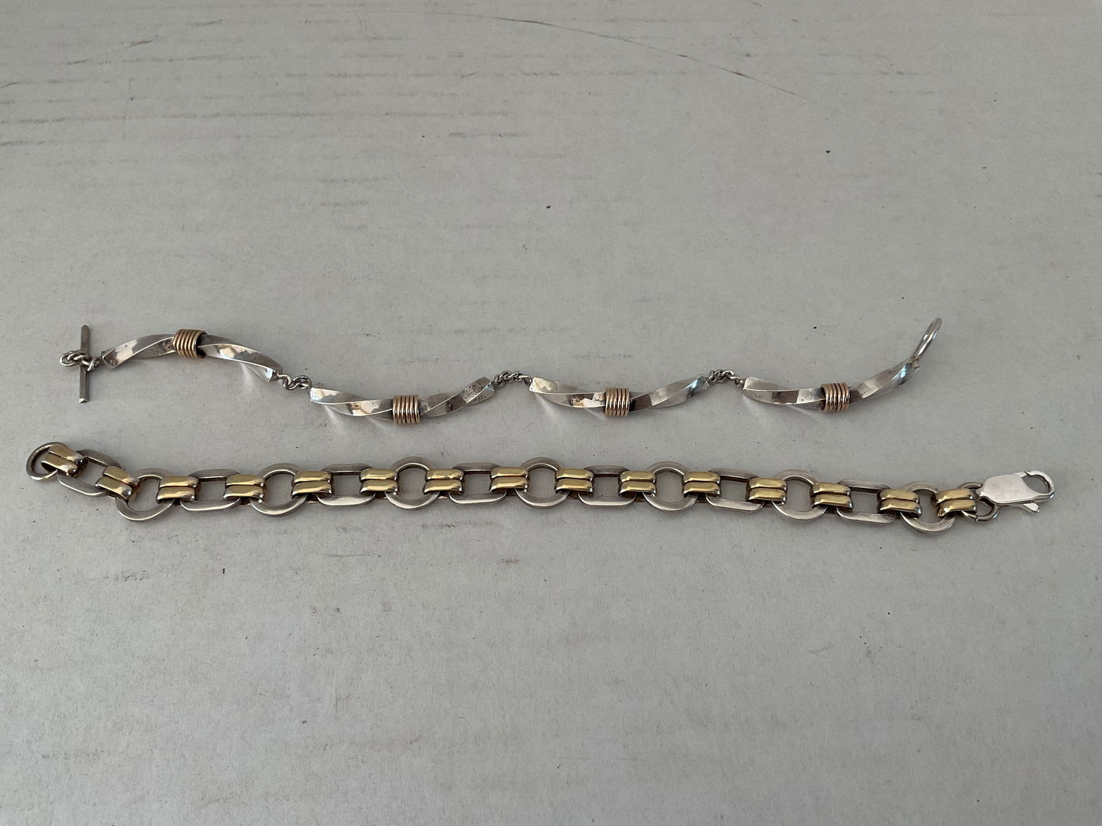 Two Sterling and 14K Yellow Gold Bracelets: Two tested sterling and 14K yellow gold bracelets. Included is a 7" toggle colsure bracelet and the other is a 7.75" lobster clasp bracelet. The lobster clasp bracelet appears to have been cut down fr