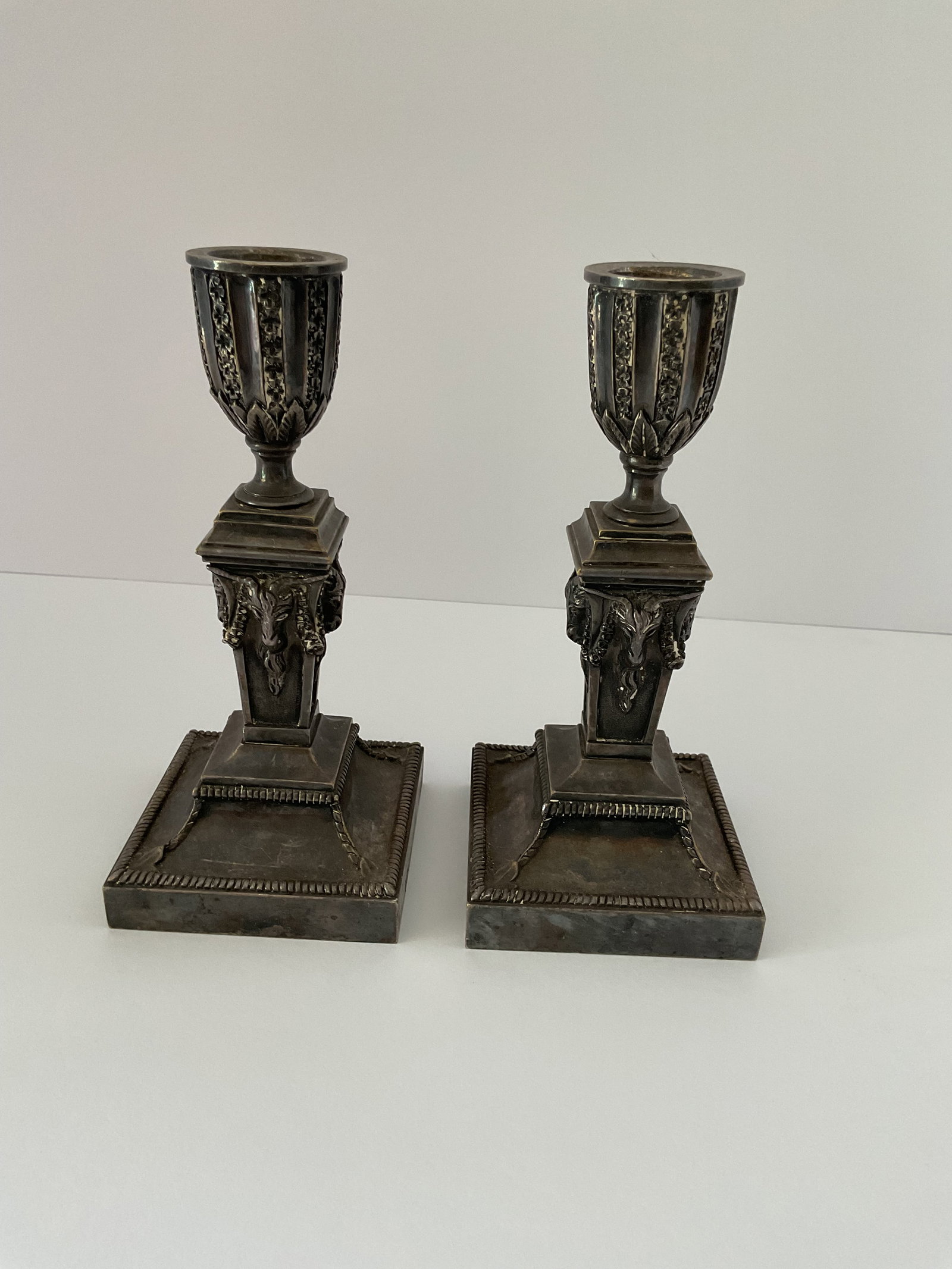 Pair of Silver Plated Bronze Neoclassical Candleholders: A pair of antique silver over bronze candleholders. These neoclassical pieces feature acapanthus leaves and masks. Late t9th to early 20th century. Each is 6.5" in height and the base is 3" square.