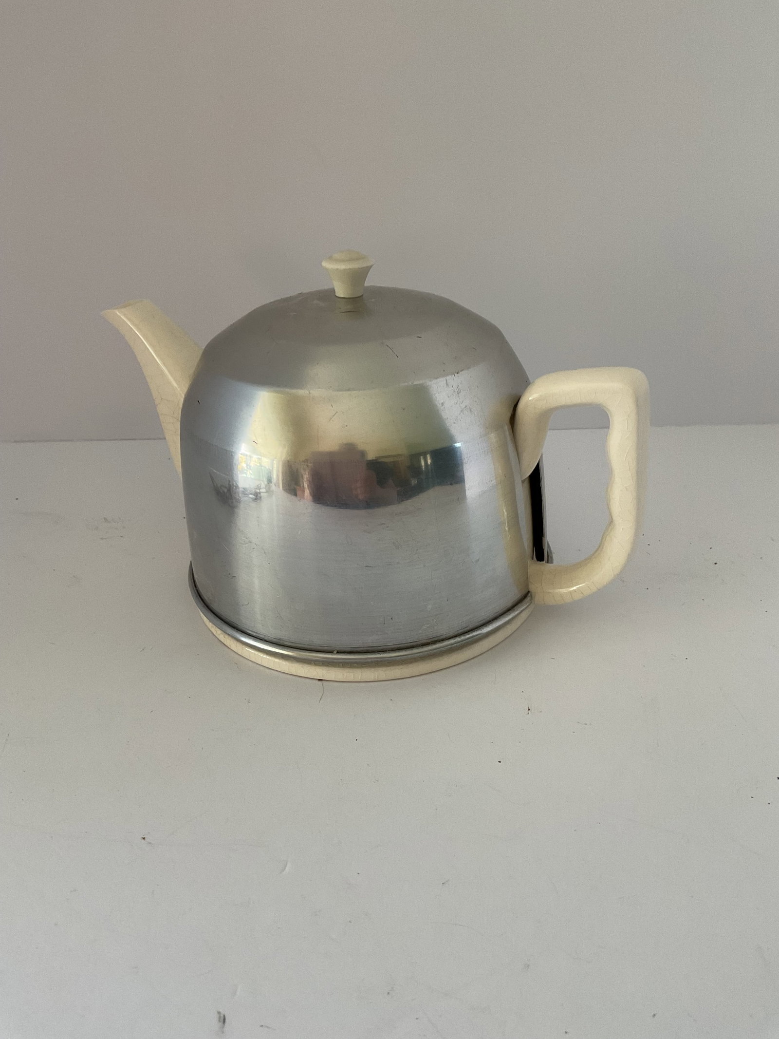 Mid Century Ceramic Teapot with Metal Heat Retainer: A cream colored ceramic teapot with a straw lined metal heat retaining cover. Some wear to the piece. It measures 10" in diameter x 8" high